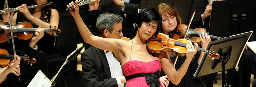 An elegantly attired violin soloist sweeps the bow high off the strings while the orchestra plays behind her
