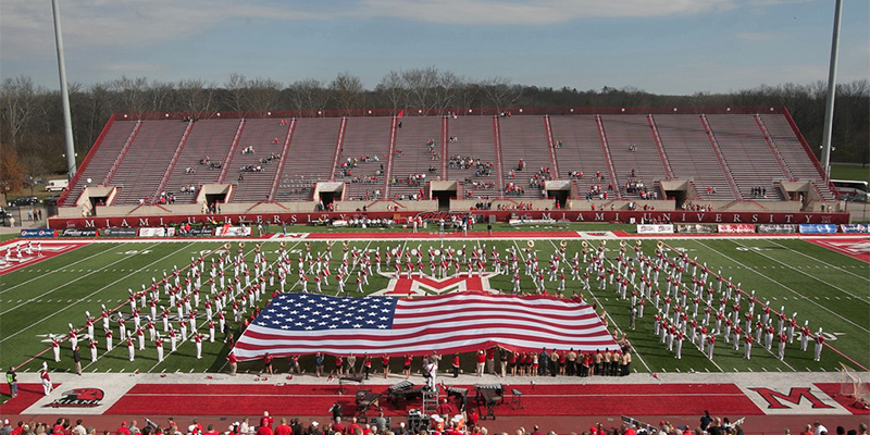 The marching band takes the field as a large American flag is displayed