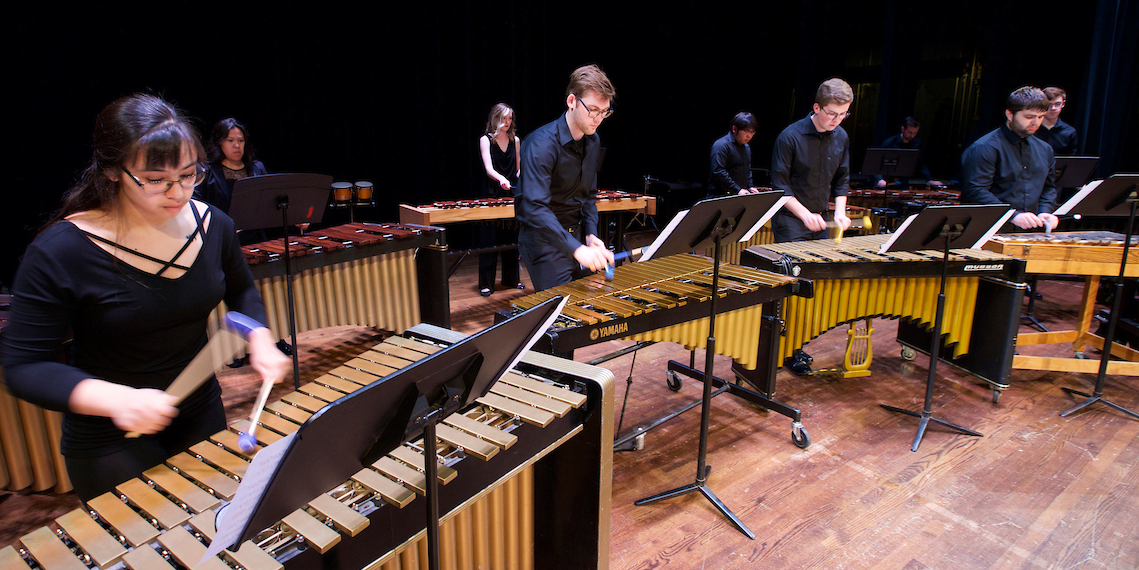  Percussion ensemble members play on a row of marimbas in concert