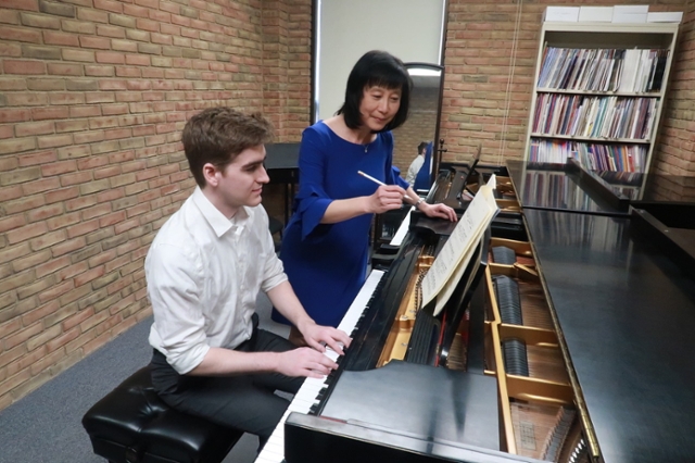 Nathan Rayens is seated at the piano as Dr. Tan instructs him in her studio