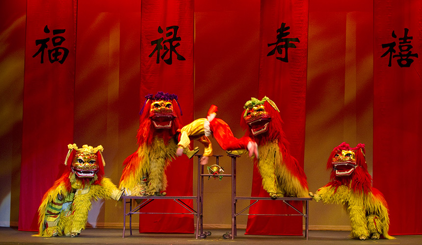 Performers in Chinese dragon costumes  moving across the stage with another performer caught in a midair flip