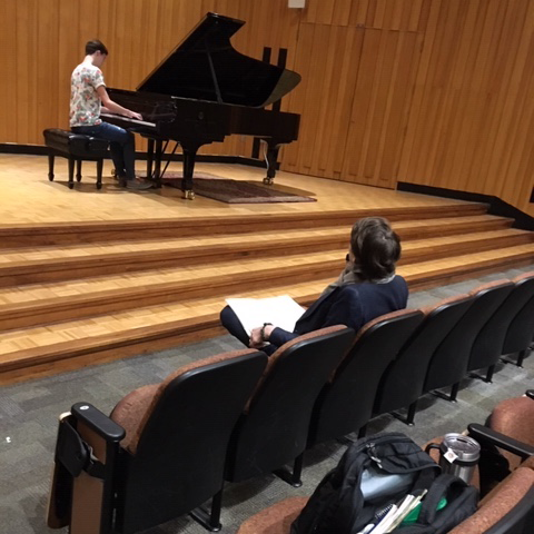Seen from behind, David Fray takes notes from the audience as a piano student performs onstage at Souers Recital Hall