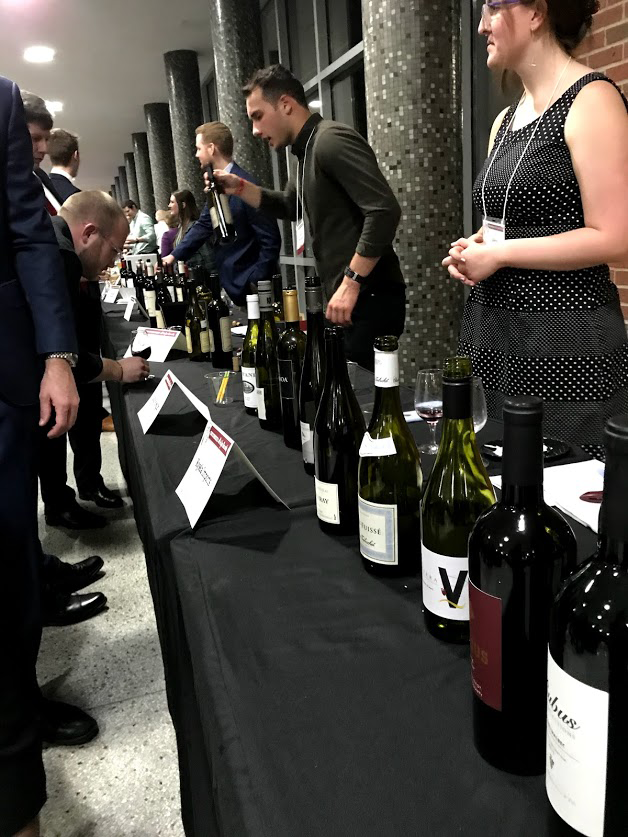People staff the wine table as guests browse the wines