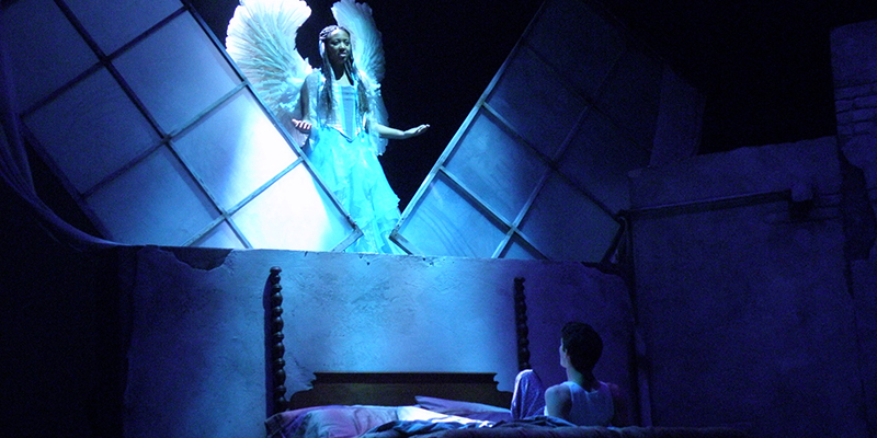 An angel hovers over a person in bed in Angels in America