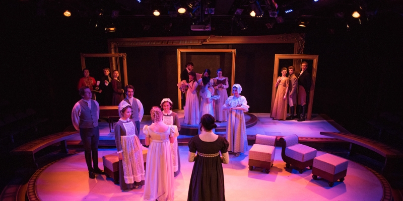  An elevated shot of a scene from a production of Pride and Prejudice, showing a romantically-lit stage with actors and actresses in period clothing