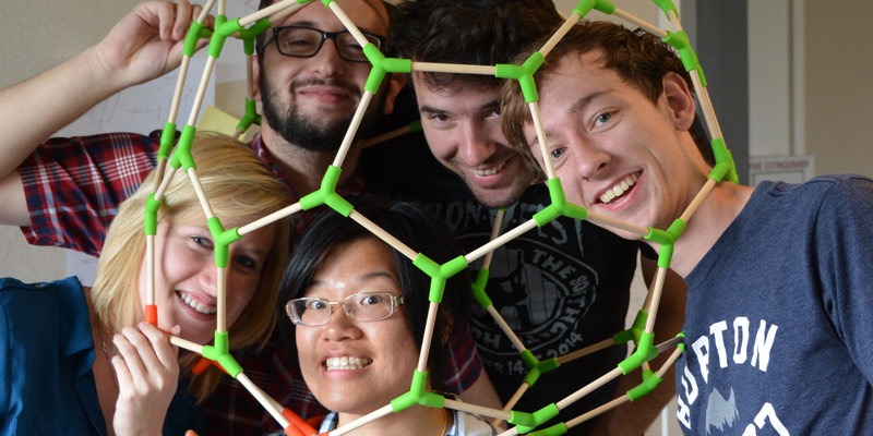  Smiling students posing with their heads inside a flexible geometric sculpture