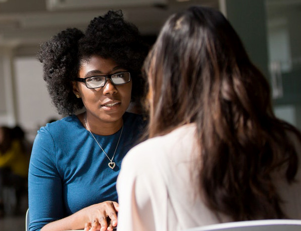 a black woman interviewing an aisian women at a table in a cafe