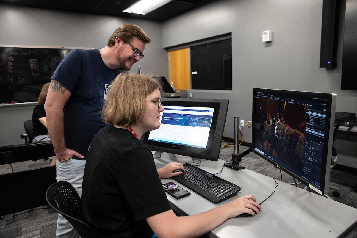 professor assisting student creating a computer game in a computer lab