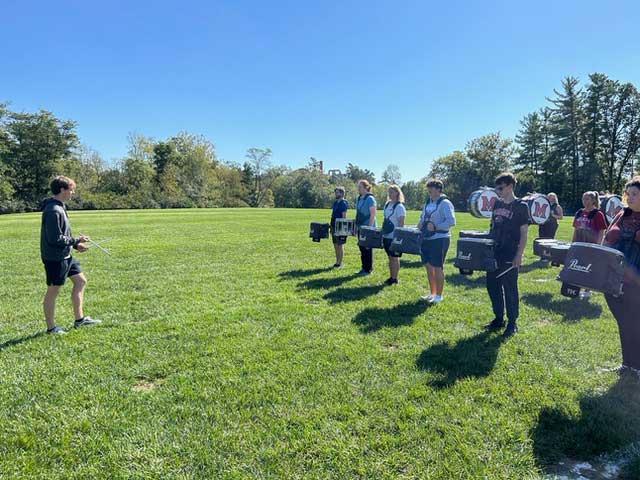 Students playing snare, bass, and marching sextet drum in a drumline