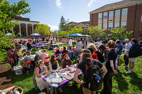 Large numbers of college students interact with various arts activities and vendors on the Arts Quad with the sun shining brightly