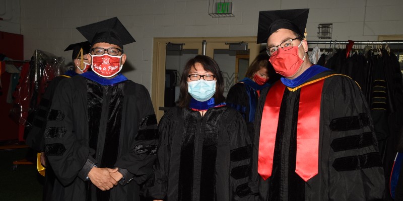 Three faculty members wearing masks before the graduation ceremony