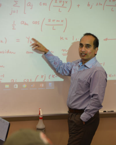 Dr. Amit Shukla in front of a white board pointing at an equation