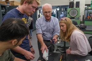 Three students gathered around a professor who is showing them an engineering material.