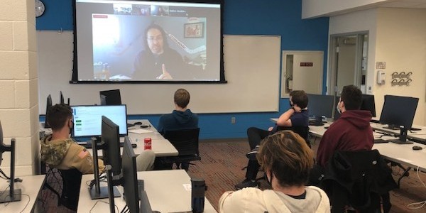 A group of students facing a Zoom session projected on a screen