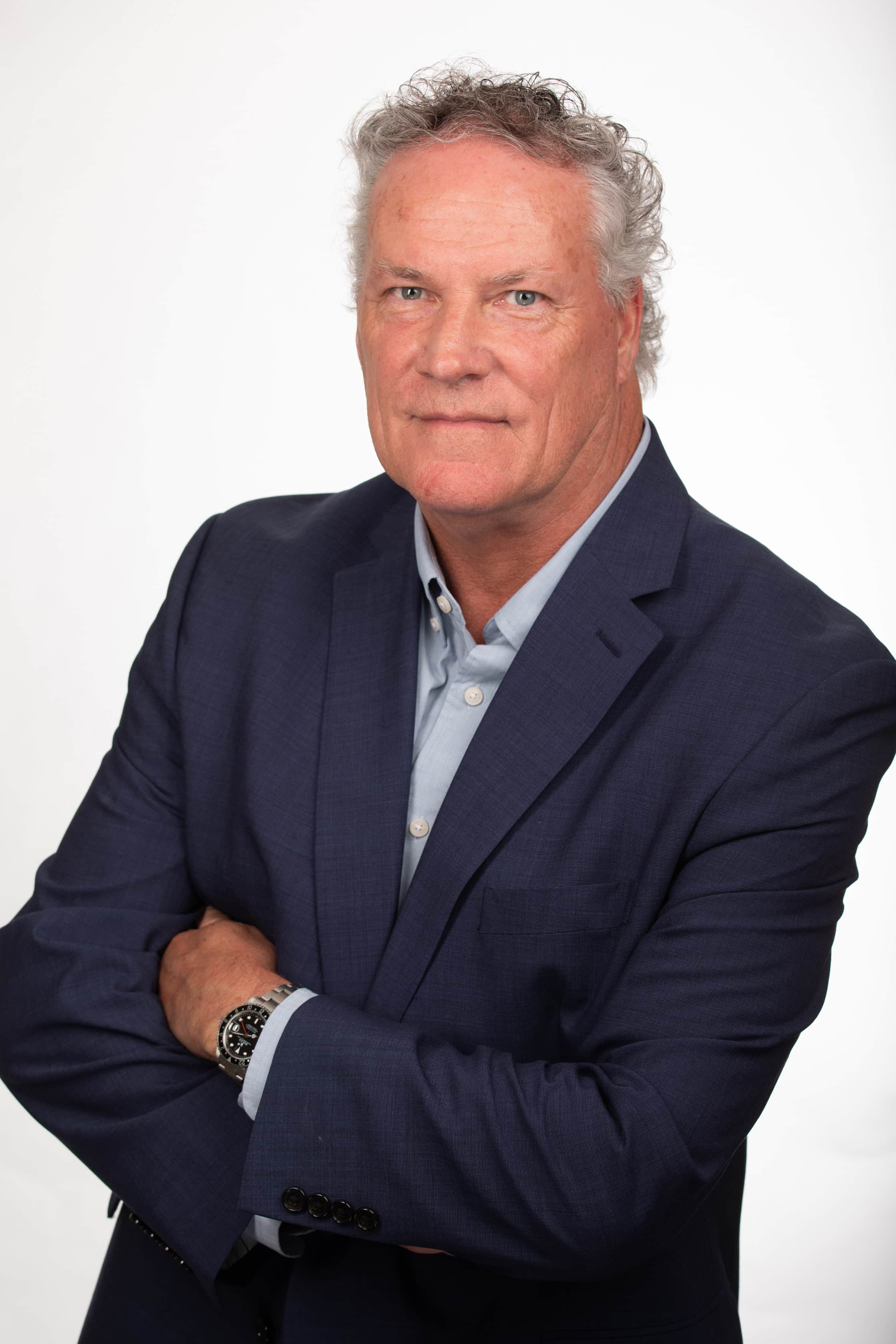 Business headshot of a middle-aged man in a navy suit with arms crossed against a white background.