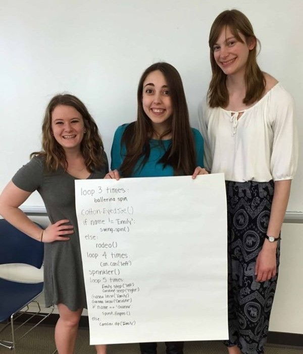 Three female students posing with a worksheet they created with computer code.