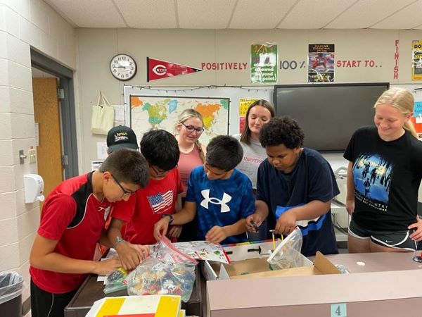 Four male students working on a project with three females standing behind them.