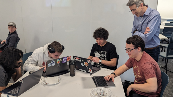 Mark Jeanmougin, cybersecurity architect, works with students at a table on a project.