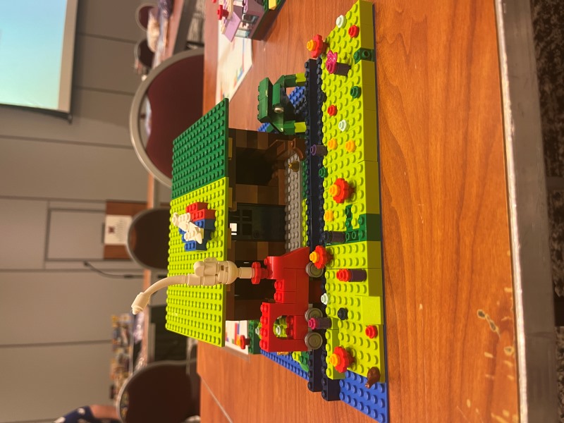 Lego build featuring a train station with a red train crossing railroad tracks