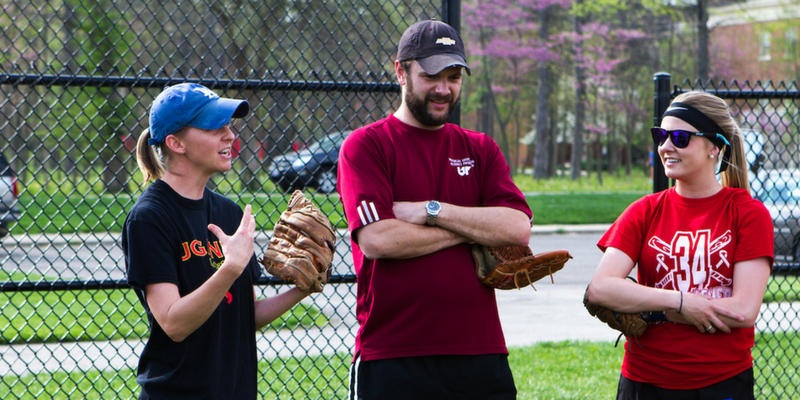 three people talk on a baseball field