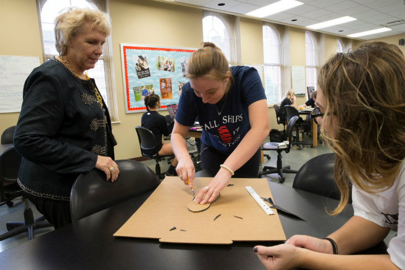 Associate Professor Ann Haley Mackenzie helps students cut out materials to build shoes