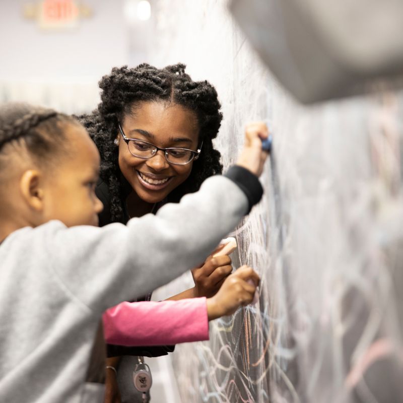 woman working with a young girl on a chalkboard