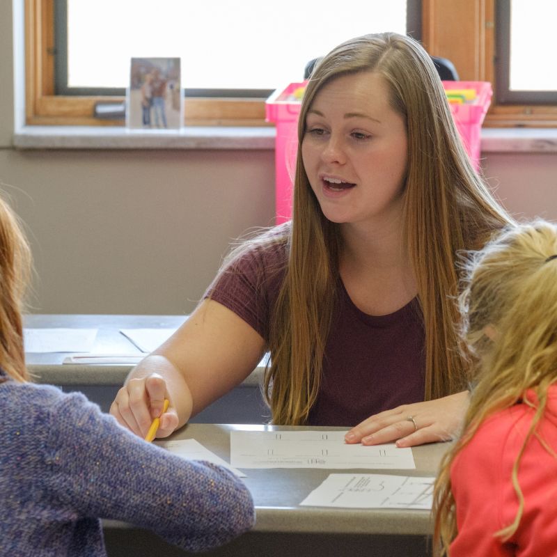 woman working with two young students at a table