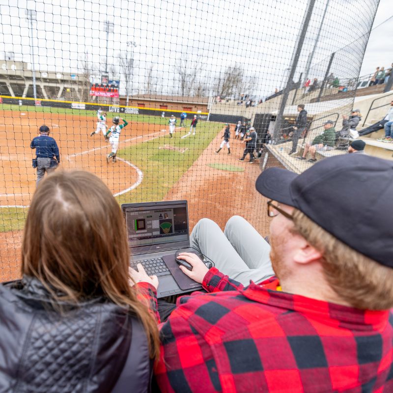 students using a laptop at a baseball game to track stats