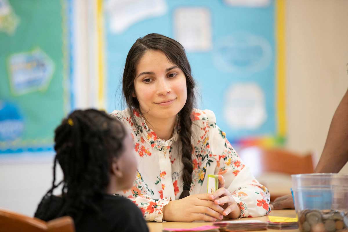 Student teacher playing a card game with a elementary student smiling