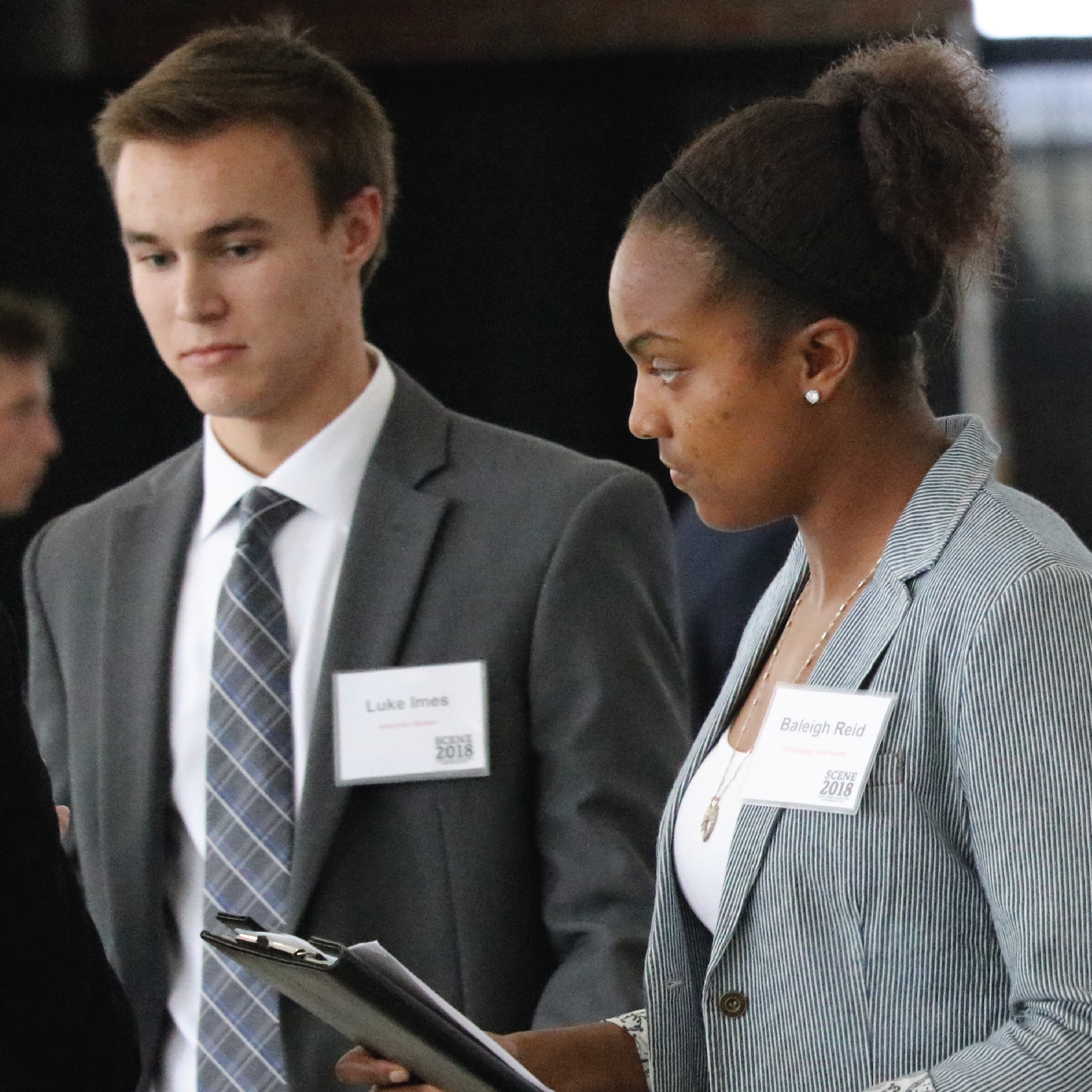 Two students dressed in suits stand in line to speak with employers.