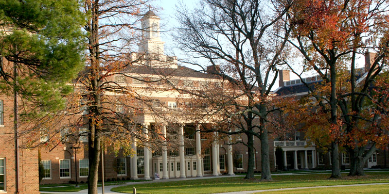 Farmer School of Business exterior in the fall. Large building with clock tower and pillars over the entrance surrounded by trees turning orange.