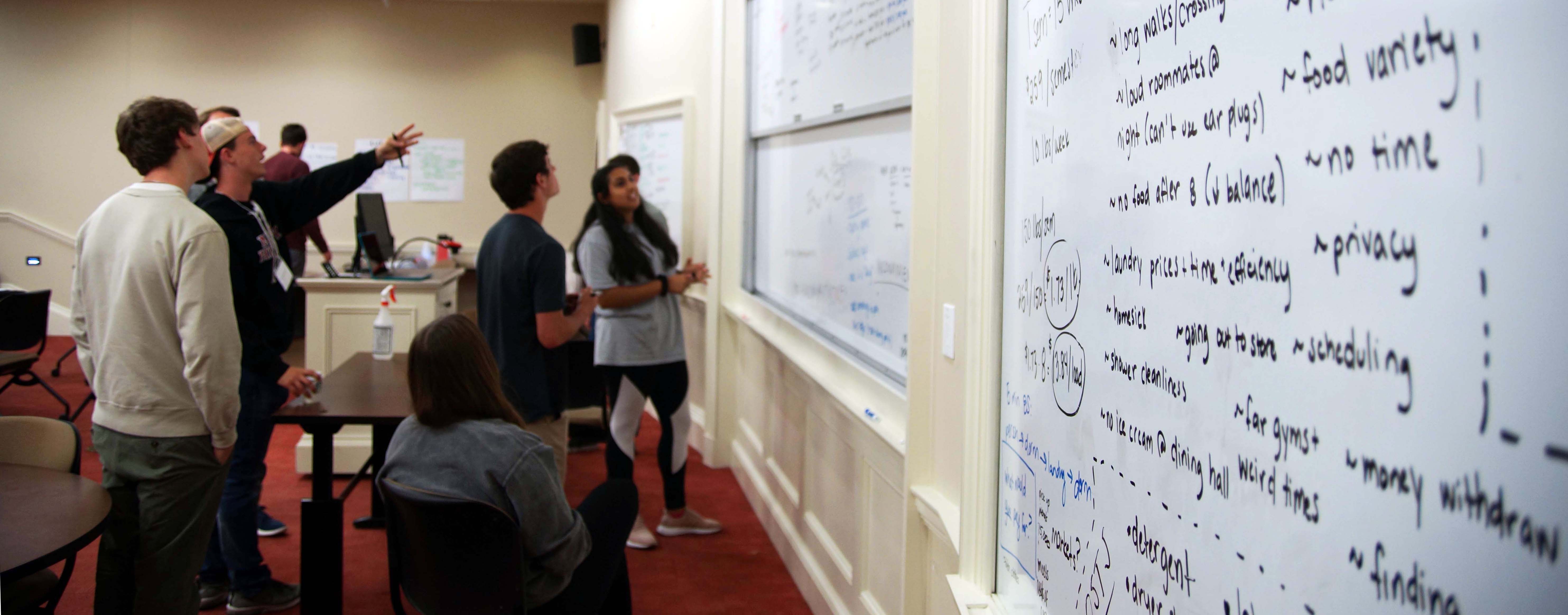 A team works on their idea at a whiteboard in a classroom