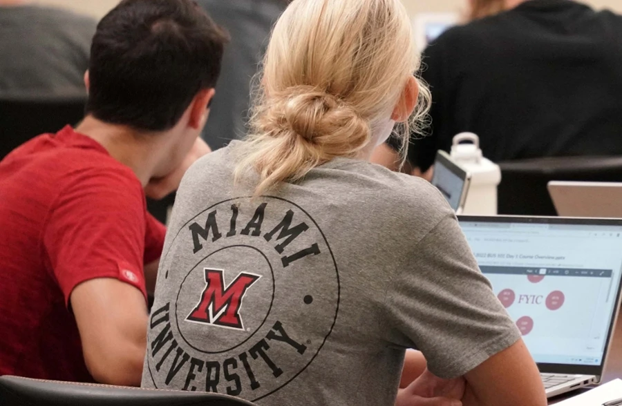 student facing front of classroom wearing a grey t shirt with  Miami University logo