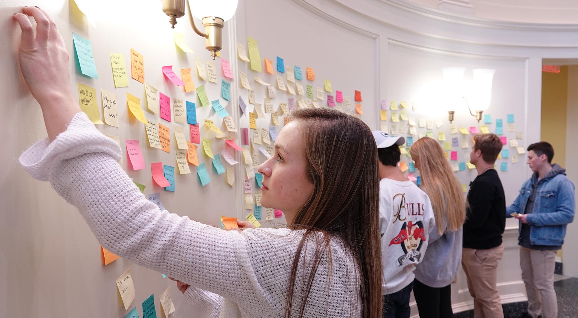 Students begin removing Post-It notes from the wall as the project ends