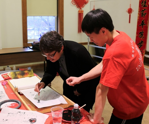  A woman writes Chinese calligraphy while a man stands over her shoulder helping her