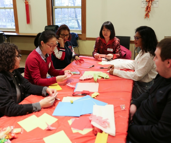  a group of people sit around a table and fold paper crafts