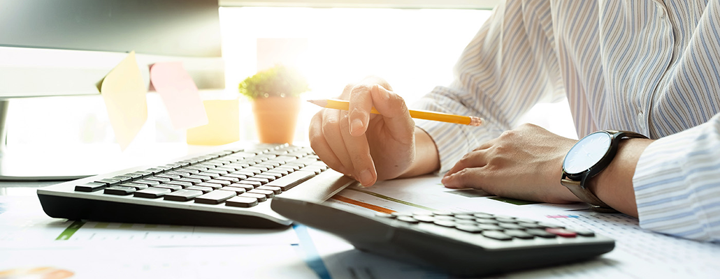 A person works with laptop, paper and calculator