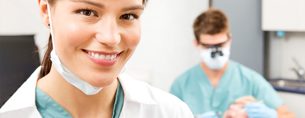 A smiling man in white coat pauses next to a smiling child in a dentist's chair