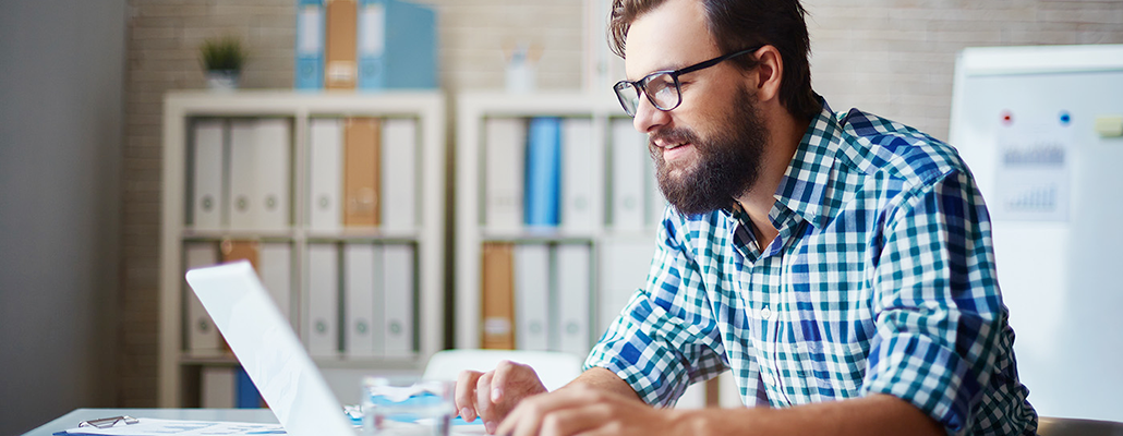 A bearded man works on a laptop