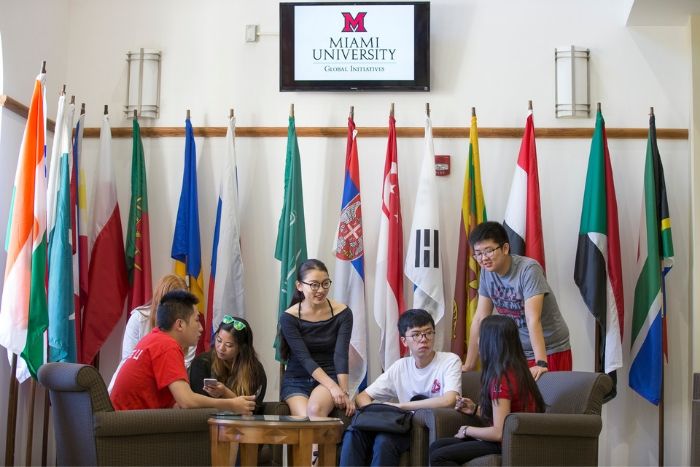 many students sitting in MacMillan Hall's lobby. Digital sign on wall with Miami logo on it.