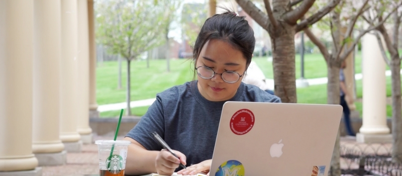 international student looking at laptop and writing in a notebook