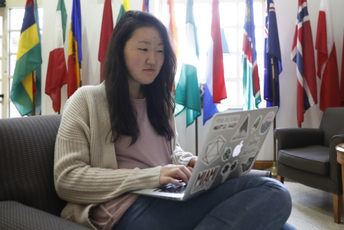 A student works on a laptop on first floor of MacMillan Hall, surrounded by international flags