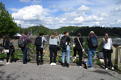 Students facing away from camera, lined up at a fence looking out at a vista