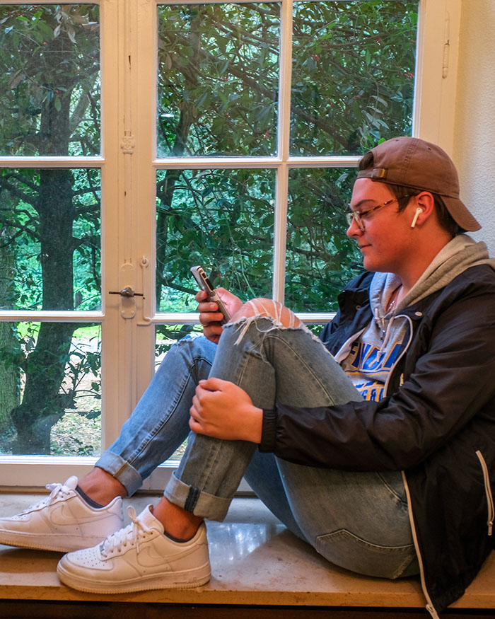 student sitting on ledge in front of window, on phone