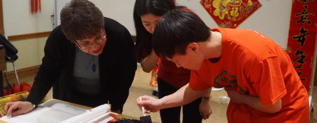 two people paint a Chinese block print while someone looks over their should, helping them