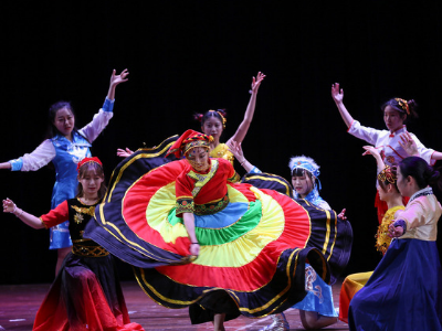 a group of students dance on stage. the girl in the middle wears a colorful skirt that twirls around her