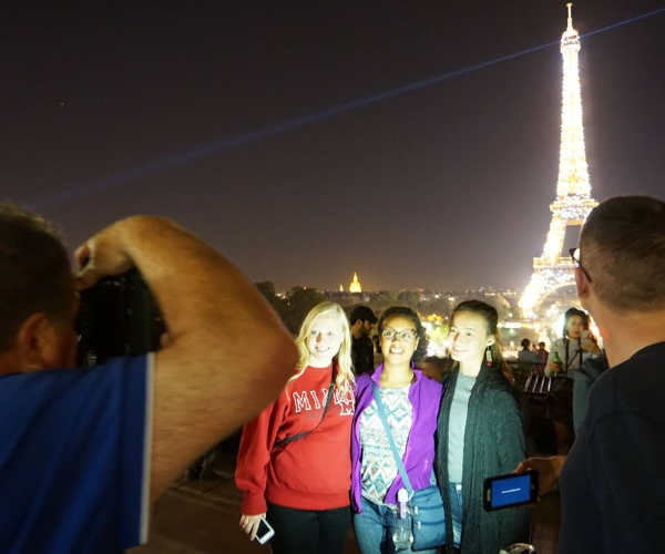 Miami photographer taking a photo of three students standing in front of the Eiffel Tower in Paris, lighting up