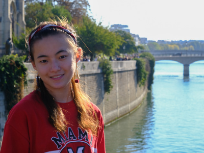 a girl smiling wearing a red Miami shirt, with a bridge and river behind her