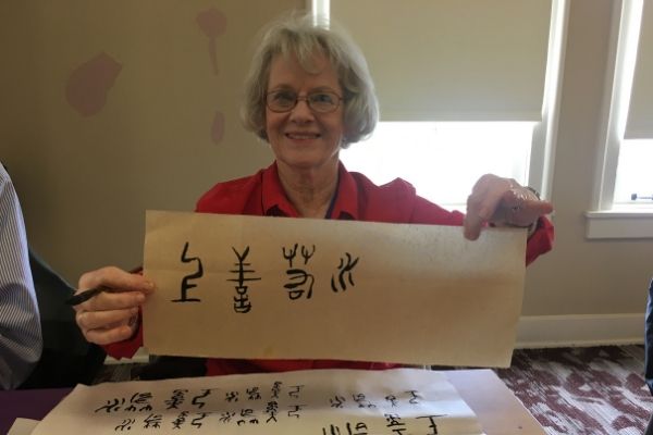 American woman holding up a paper with Chinese characters she drew on it in black ink