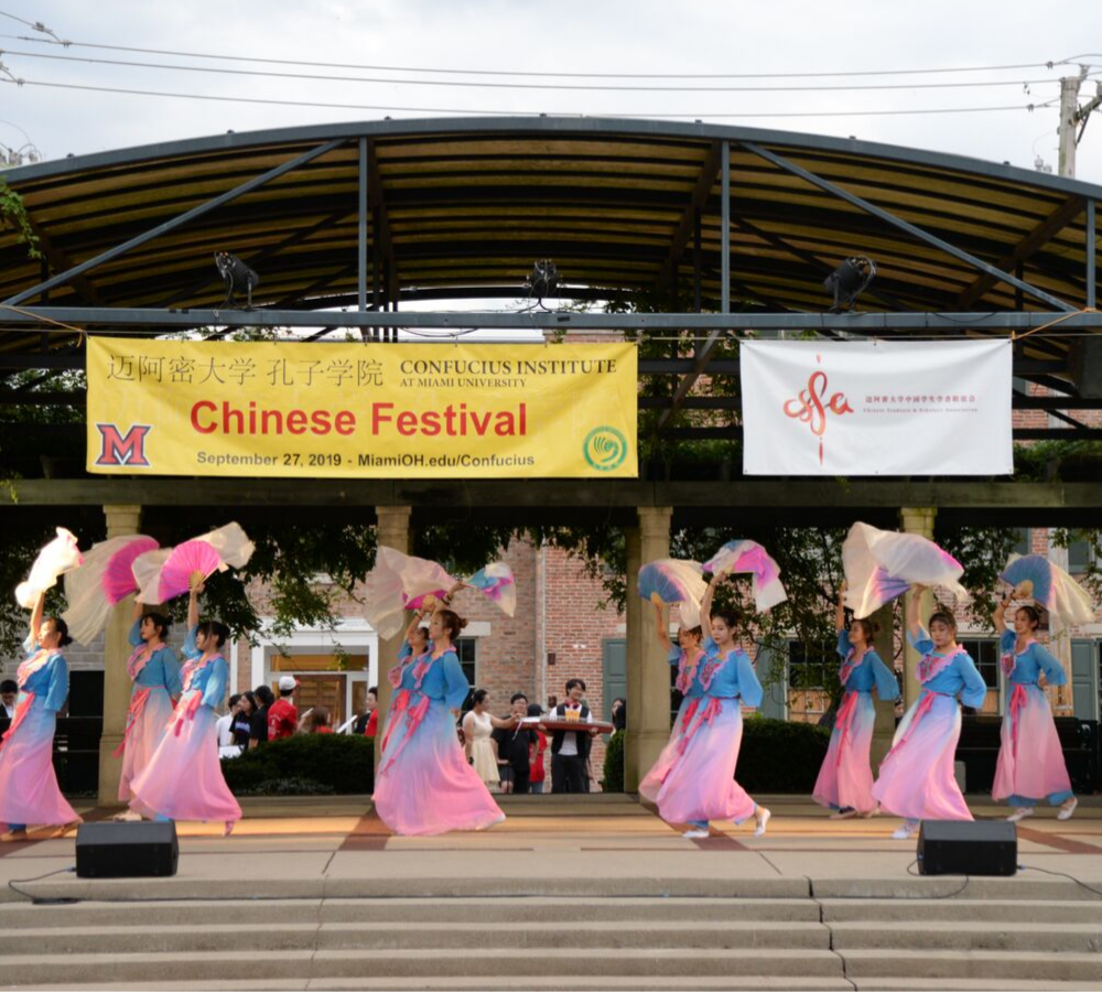 Students wearing blue and pink costumes dance on stage